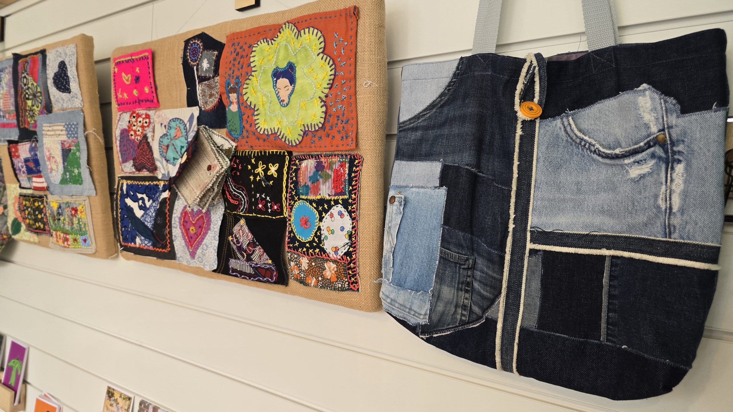 Exposition on the wall of patches made from scraps fabrics and a denim bag made form pieces of old jeans.